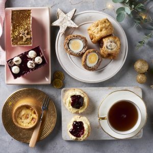 scotch eggs, susasage rolls and cakes on plate with star and baubles with christmas lights
