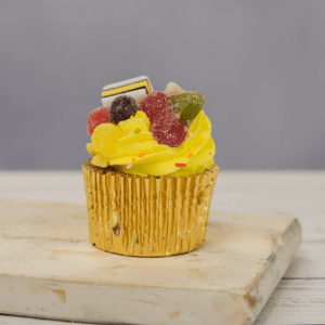 A cupcake with yellow frosting, covered in sweets, sat on a white chopping board.