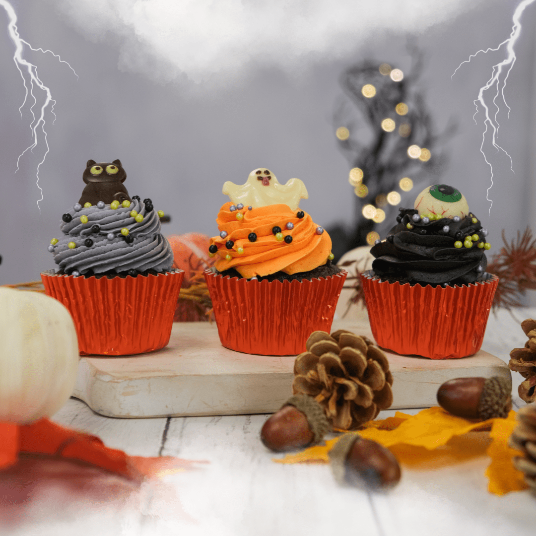 Three halloween cupcakes from our selection box, surrounded by spooky decorations